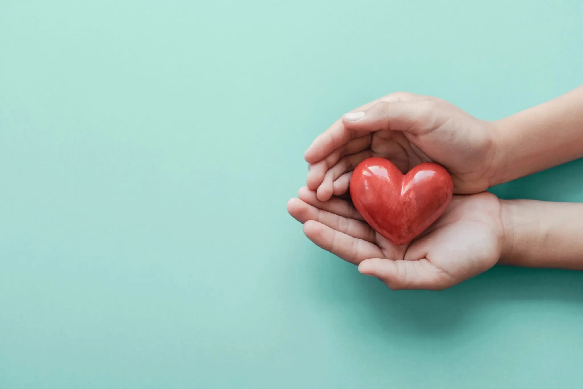 hands holding red heart blue background scaled 1